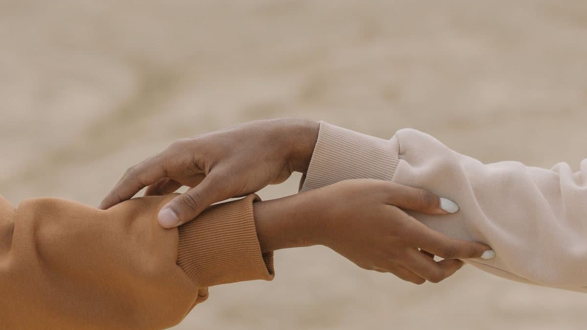 Deux mains qui se rejoignent et se tiennent l’avant-bras, sur un fond sable