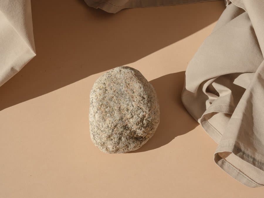 Un galet posé sur un drapé de toile beige, ombres douces